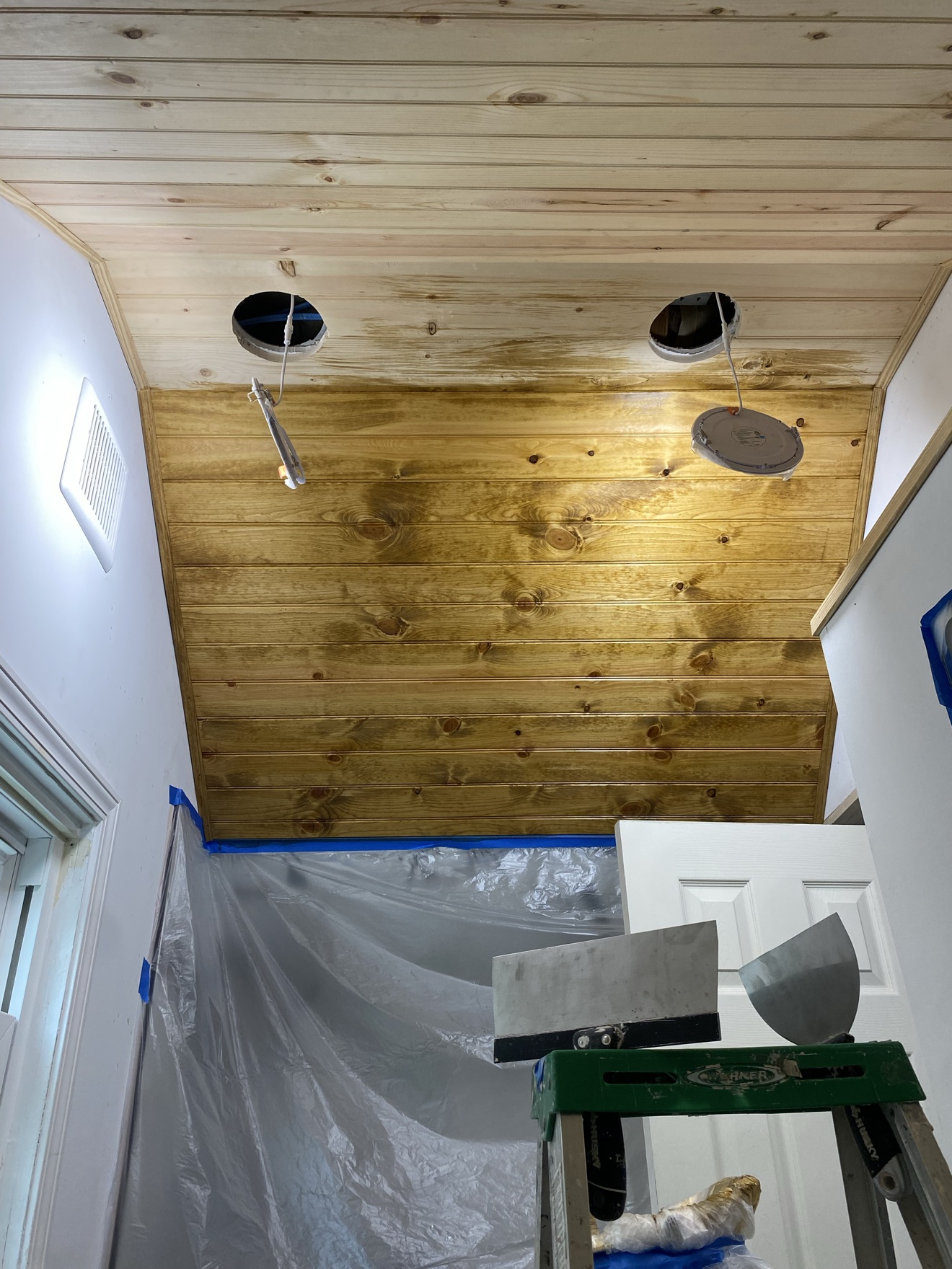 Bathroom wood-plank ceiling mid-stain — half natural pine, half stained, light fittings not yet installed