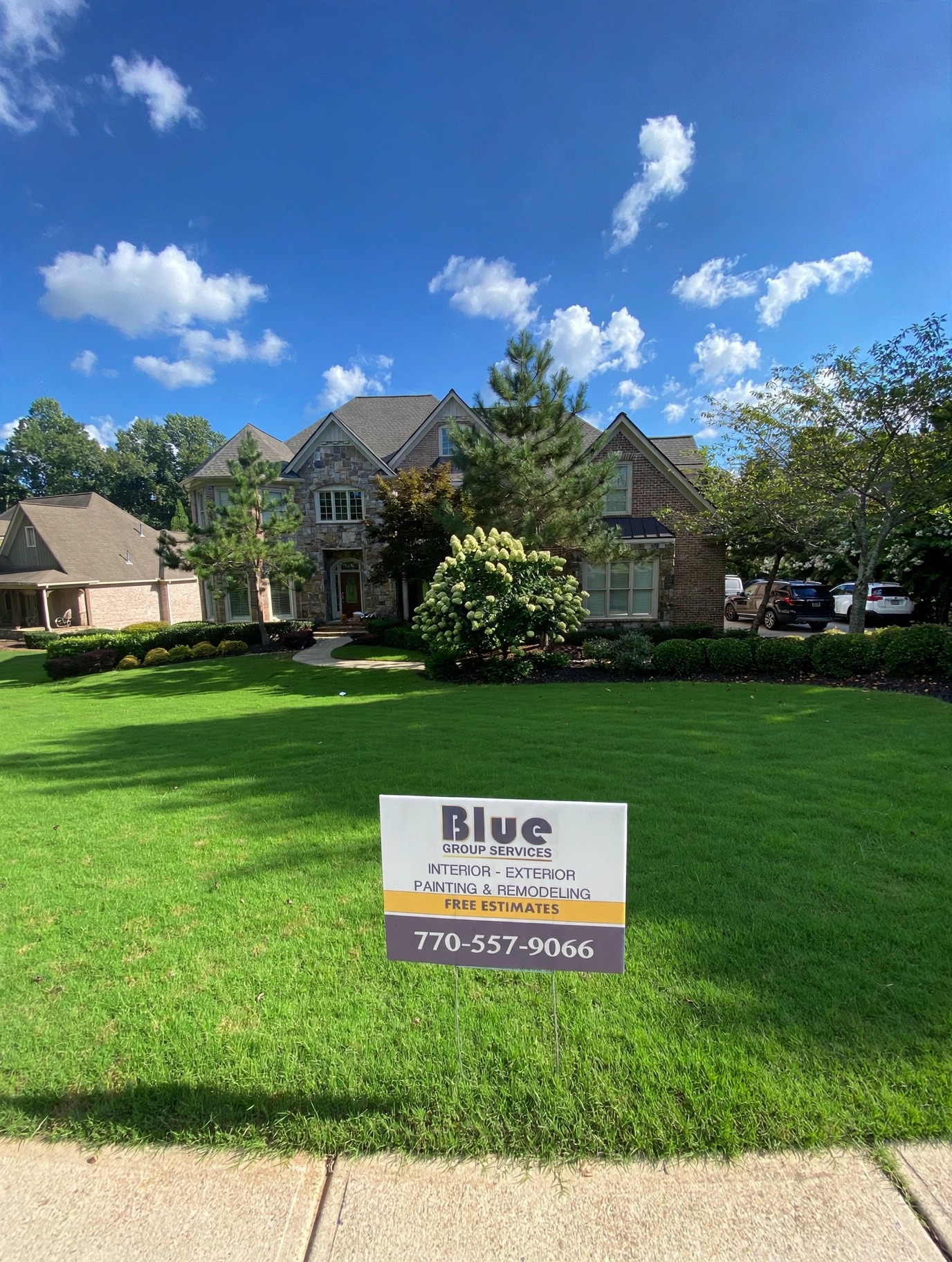 Stone and brick home with a manicured front lawn and a Blue Group Services yard sign with our number, 770-557-9066