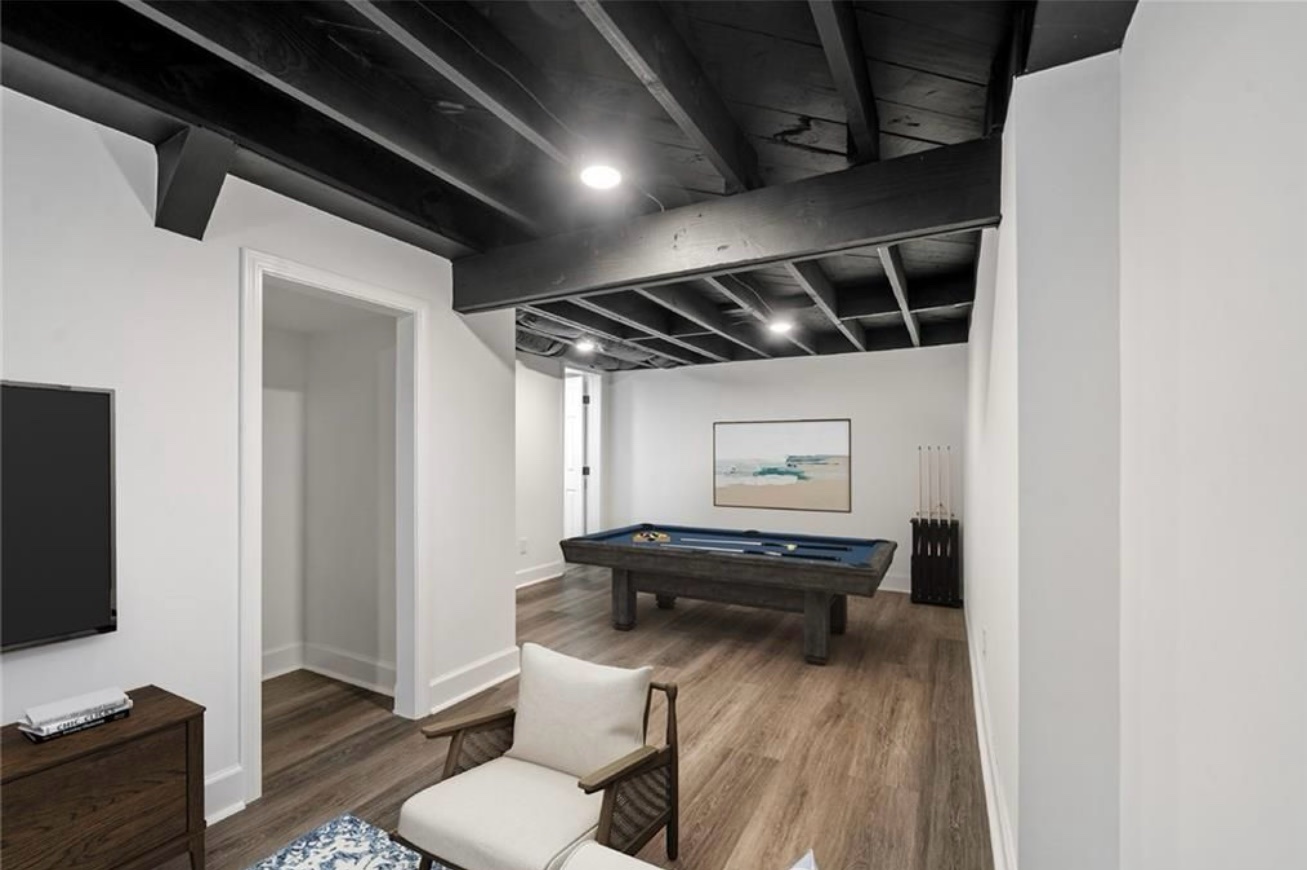 Finished basement game room with white walls, a black painted beam ceiling and a pool table