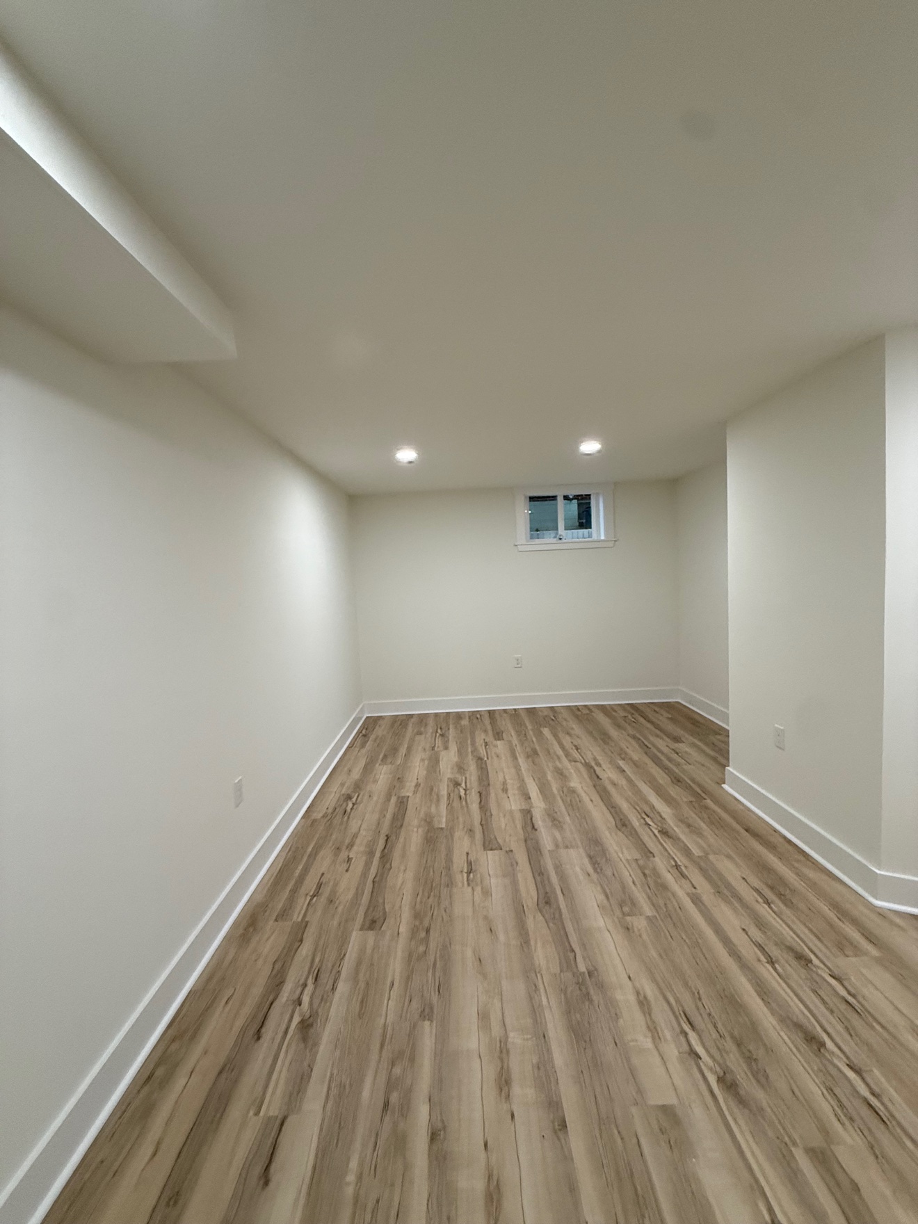 Finished basement room with fresh white walls and wood-look floors