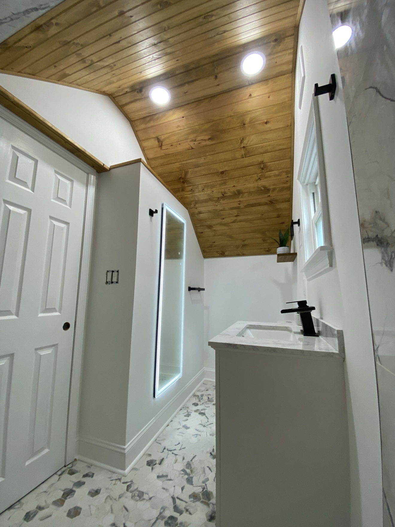 The same bathroom finished — stained wood ceiling sealed, backlit mirror and marble-look hex floor