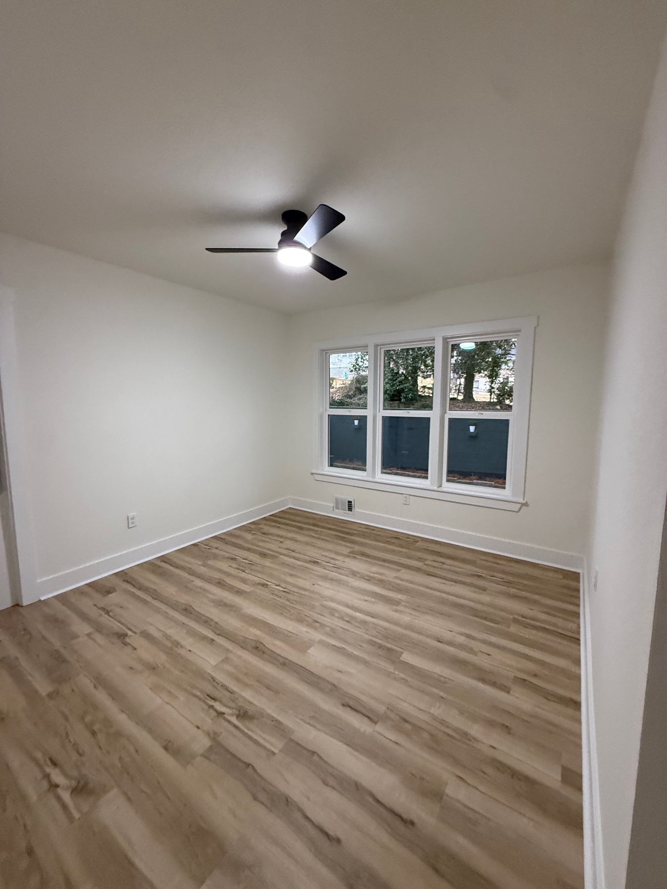 Freshly painted bedroom with clean white walls, wood-look floors and a ceiling fan