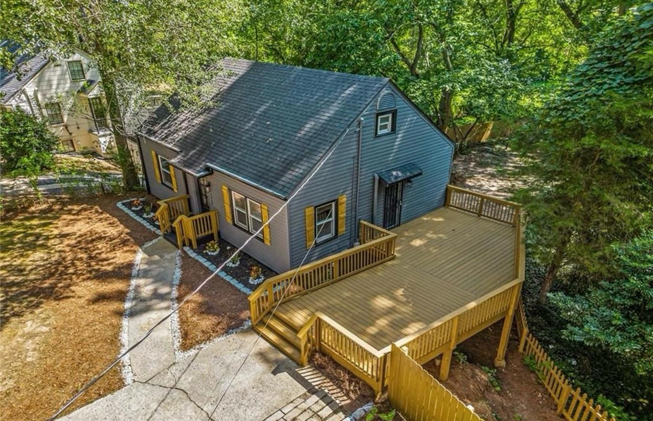 Aerial view of the gray repainted home with natural wood shutters and its large new wood deck