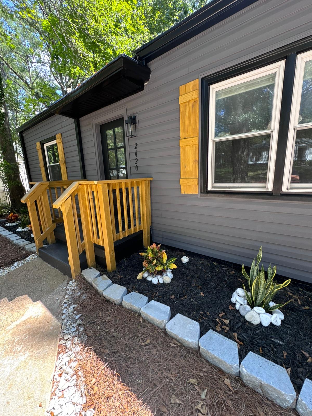 Gray home exterior with black trim, natural wood shutters and a new wood porch railing with fresh landscaping